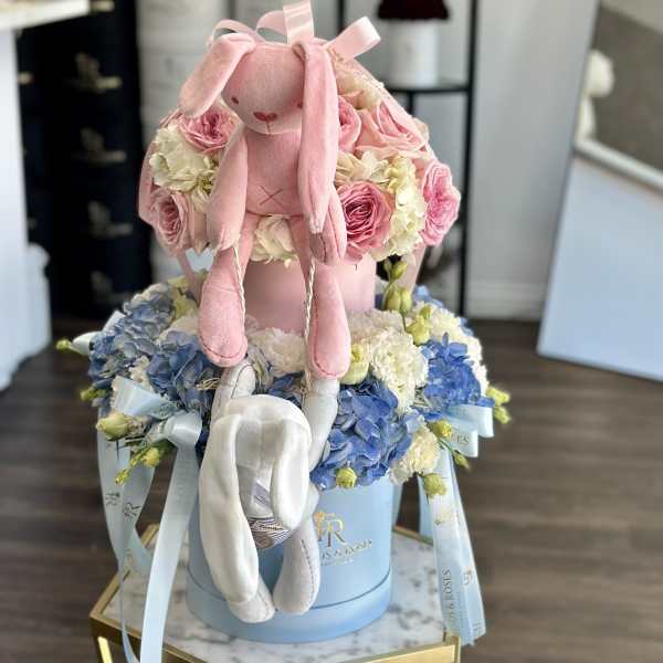 Pink plush bunny sitting on a box of pink and blue flowers