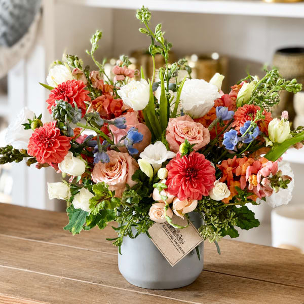 Mixed bouquet of coral, white, and blue flowers in a gray vase