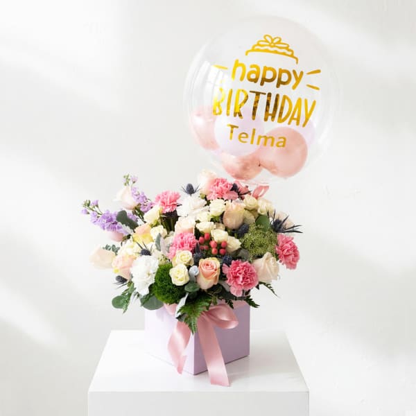 Pink and white flower arrangement with a birthday balloon in a gift box