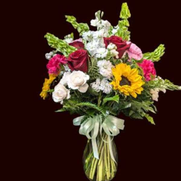 Mixed bouquet in a glass vase with roses, sunflowers, and white blooms