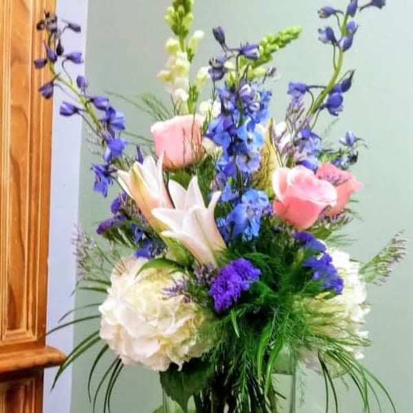 Mixed bouquet in a clear glass vase with pink roses, white lilies, and blue flowers