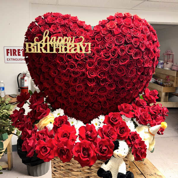 Heart-shaped red rose arrangement with a gold happy birthday sign and plush toys