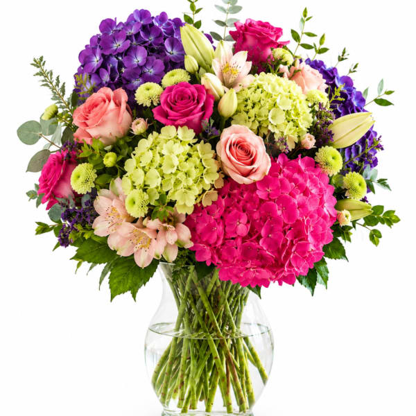Mixed bouquet of pink, purple, and cream flowers in a clear glass vase