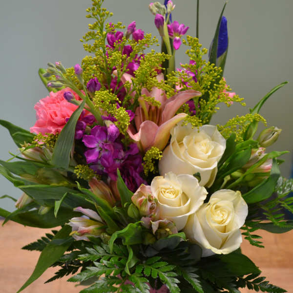 Mixed bouquet of white roses, pink lilies, and purple flowers in a pink vase