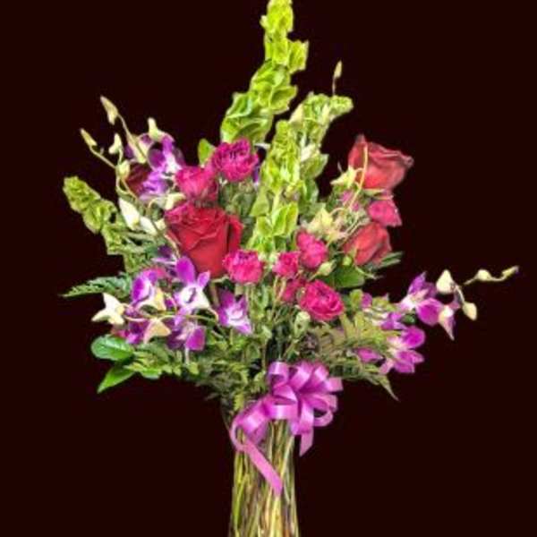 Mixed bouquet of pink and purple flowers in a glass vase with a ribbon