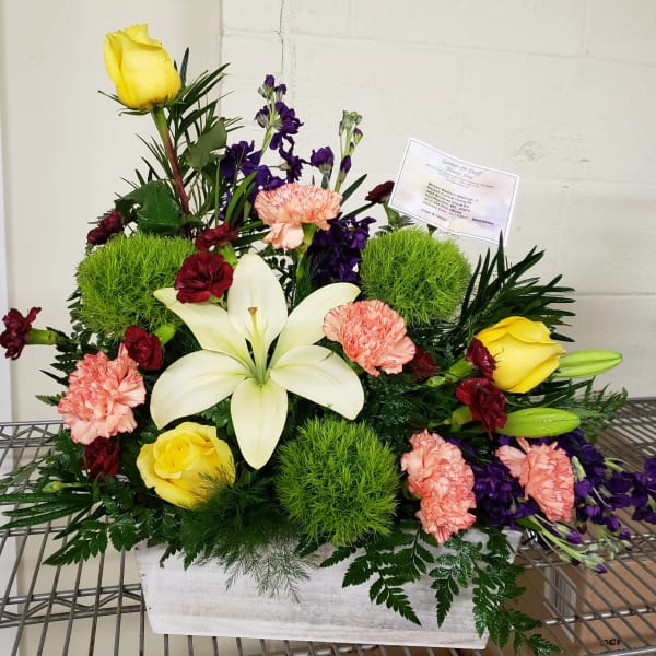 Mixed floral arrangement with yellow roses, white lilies, and pink carnations in a white container
