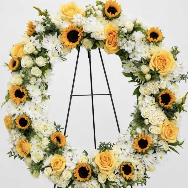 Heart-shaped floral wreath with yellow roses, white flowers, and sunflowers on an easel