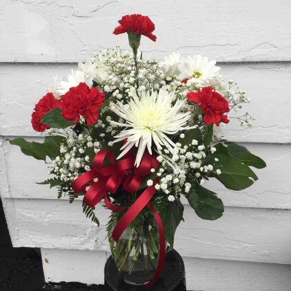 Bouquet of red carnations and white daisies in a glass vase with a red ribbon