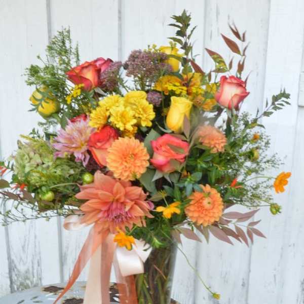 Mixed bouquet of roses, dahlias, and yellow blooms in a glass vase