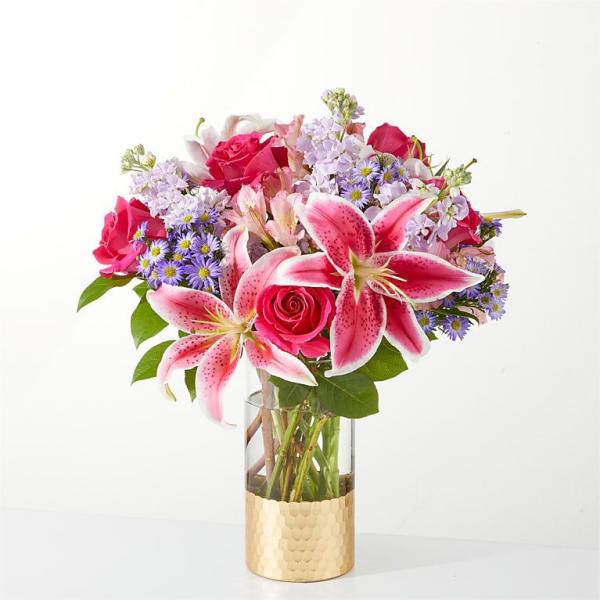 Pink lilies and roses in a clear glass vase with a gold base