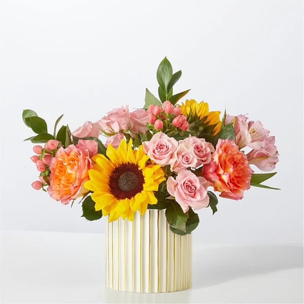 Mixed bouquet with a sunflower, pink roses, and orange blooms in a striped vase.