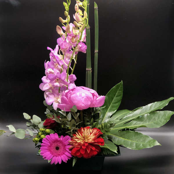 Pink orchids and mixed flowers arranged in a black container