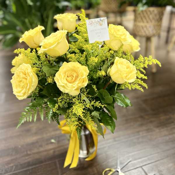 Yellow roses arranged in a glass vase with yellow ribbon