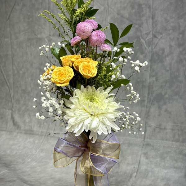 Tall bouquet of yellow and white flowers in a glass vase with a ribbon bow