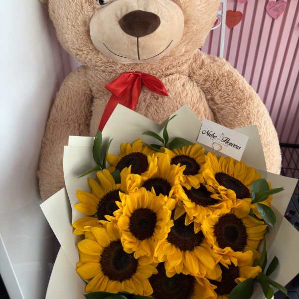 Teddy bear holding a bouquet of sunflowers with a red ribbon