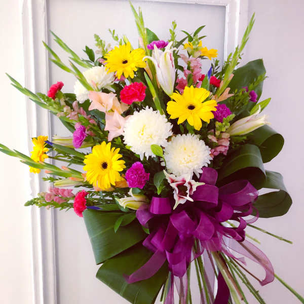 Colorful mixed bouquet with yellow daisies, white lilies, and a purple ribbon