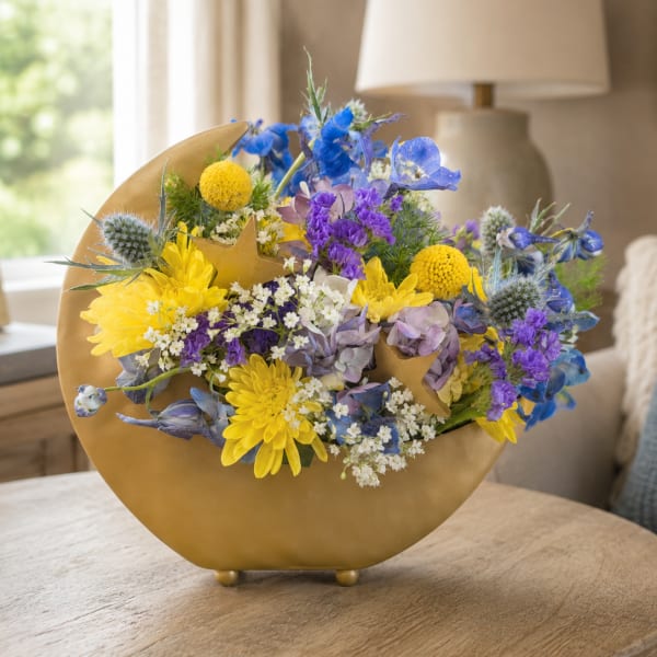 Mixed bouquet in a gold crescent vase with yellow, blue, and purple flowers