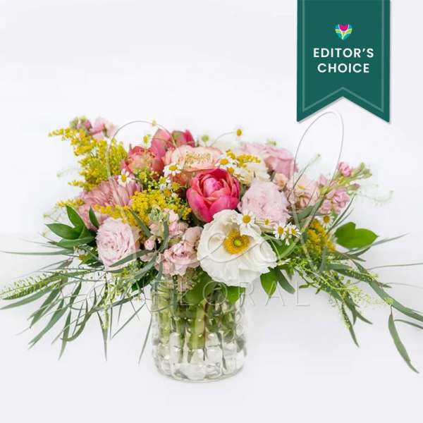 Low mixed bouquet of pink and white flowers with yellow accents in a clear glass vase.