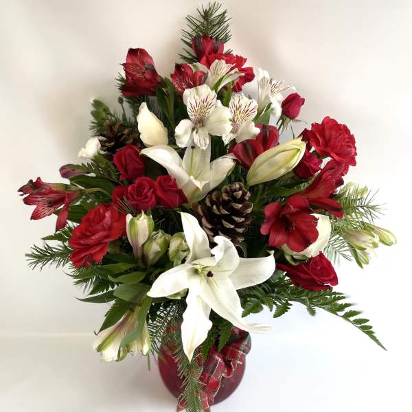 Red and white floral arrangement in a red vase with pinecones