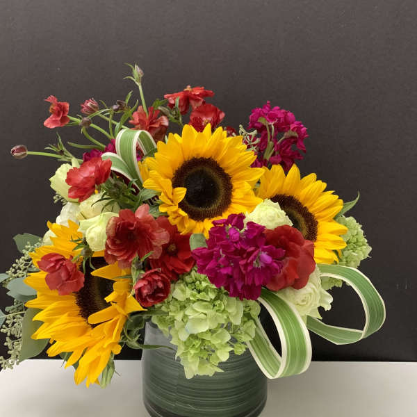 Mixed bouquet with sunflowers, hydrangeas, and red blooms in a dark vase