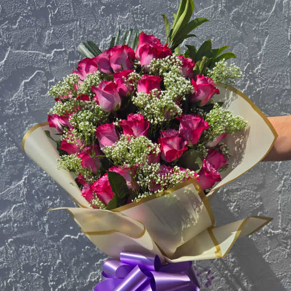 Bouquet of pink roses with white filler flowers and a purple ribbon