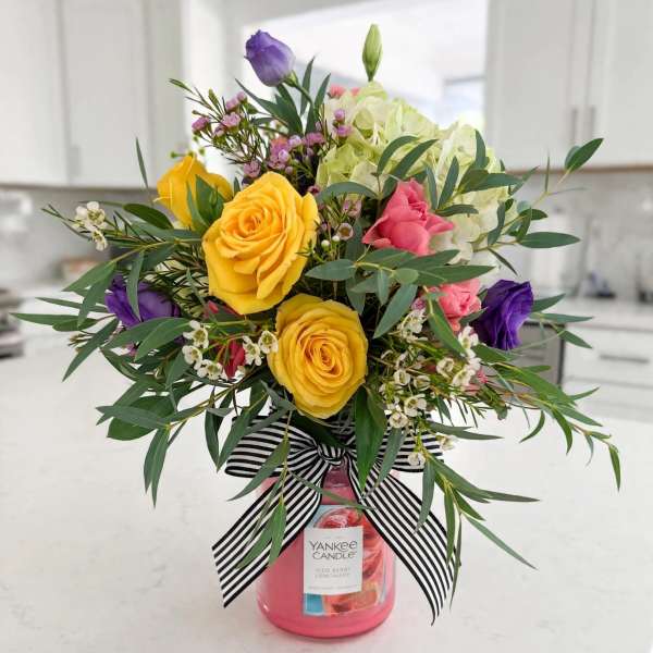 Bouquet of yellow, pink, purple, and white flowers in a pink candle jar