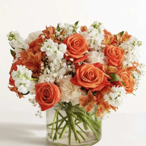 Orange roses and white flowers arranged in a clear glass vase