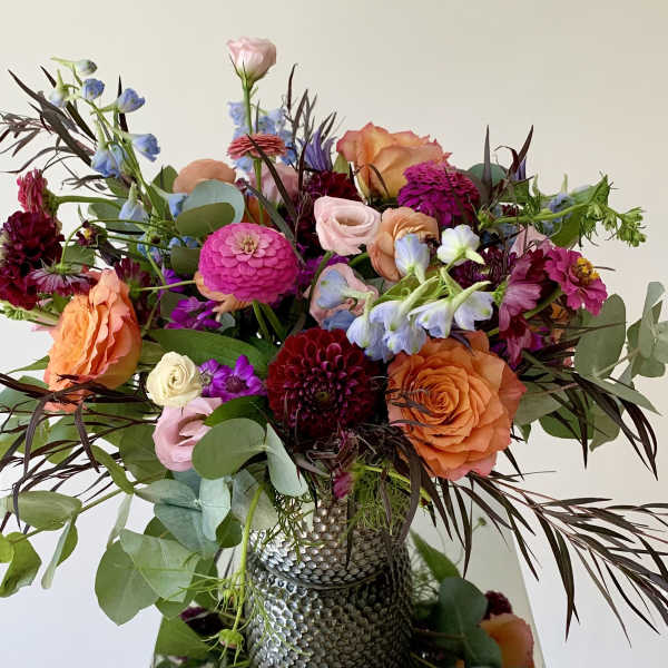 Mixed bouquet of orange, pink, and purple flowers in a textured vase