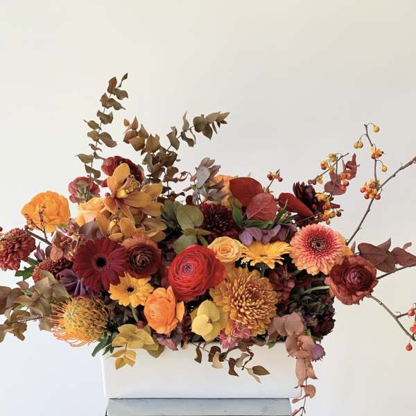 Autumn floral arrangement in a white rectangular vase with orange, red, and yellow blooms