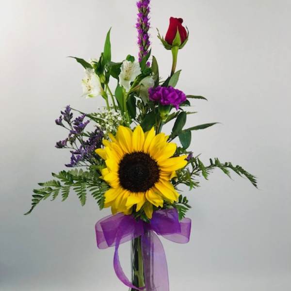 Sunflower bouquet in a clear glass vase with purple ribbon