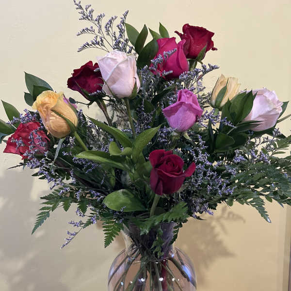 Mixed roses in a clear glass vase with purple filler flowers