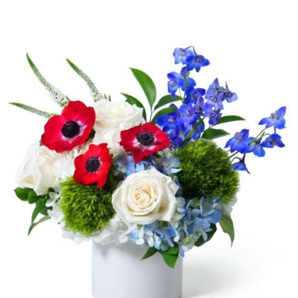 Low red, white, and blue flower arrangement with roses and anemones in a white cylinder vase