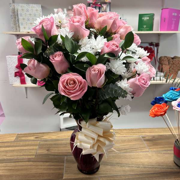 Pink roses and white daisies arranged in a vase with a ribbon bow.
