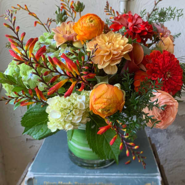 Mixed bouquet of orange, red, and peach flowers in a glass vase