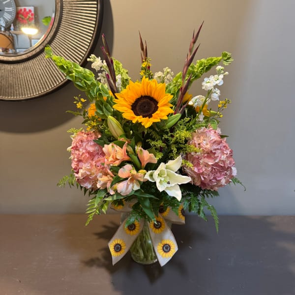 Mixed bouquet with a sunflower, pink hydrangeas, lilies, and a glass vase