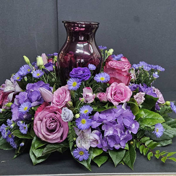Purple and pink floral arrangement around a dark glass vase