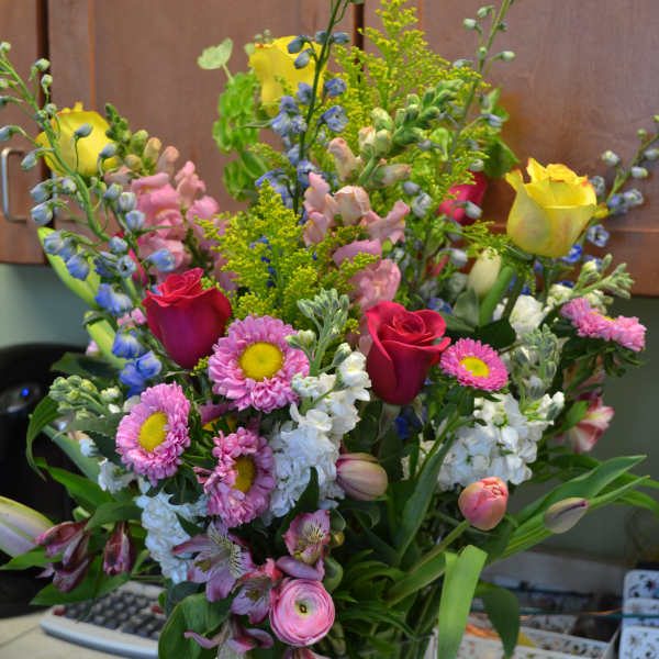 Mixed bouquet of roses, daisies, and snapdragons in a glass vase