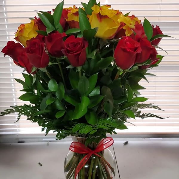 Bouquet of red and yellow roses in a clear glass vase with a red ribbon