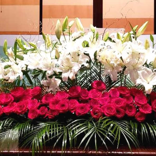 Large stage arrangement of red roses and white lilies with palm fronds in a long, low display