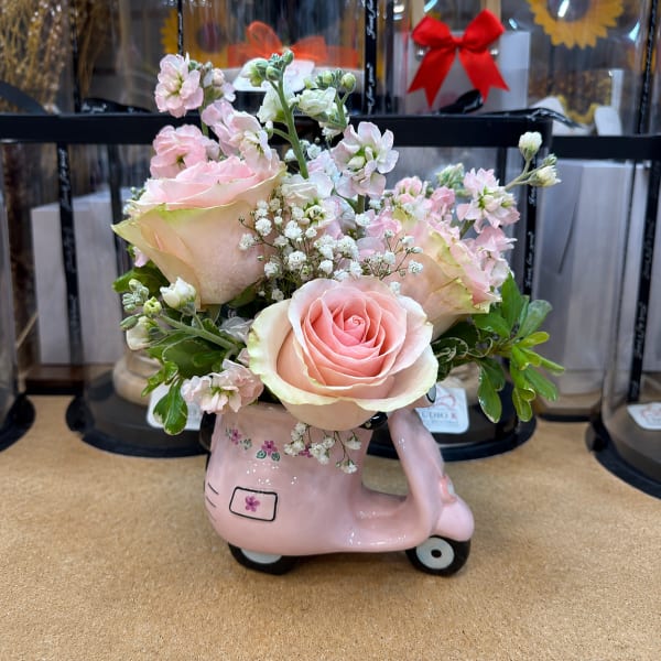 Pink roses and small white flowers arranged in a pink scooter-shaped vase
