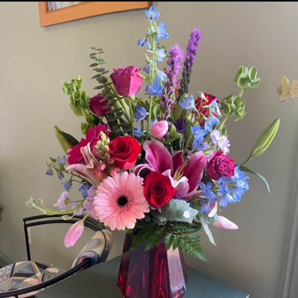 Mixed bouquet of roses, lilies, and blue flowers in a red vase