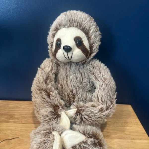 Plush sloth toy sitting on a wooden surface