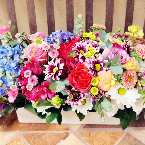 Colorful mixed flower arrangement in a white rectangular container