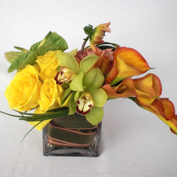 Yellow roses and orange calla lilies in a square glass vase
