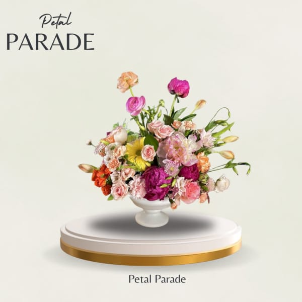 Mixed pink, peach, and yellow flowers arranged in a white pedestal vase
