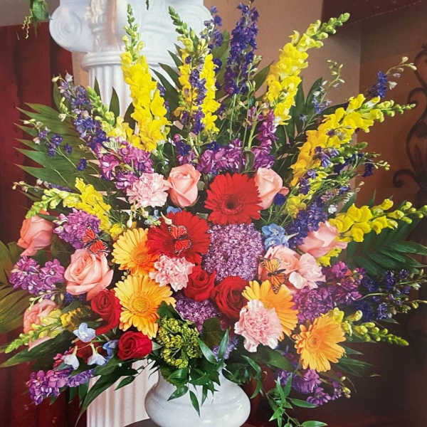 Tall mixed arrangement of bright roses, gerbera daisies, carnations and snapdragons in a white vase.