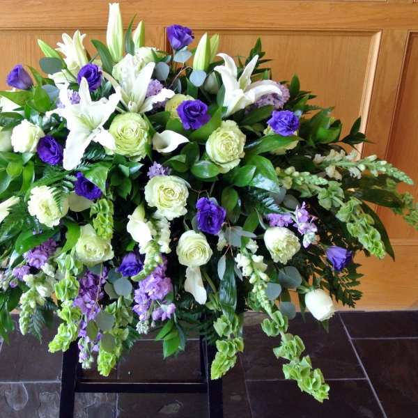 Large floral spray with white lilies, roses, and purple blooms on a stand