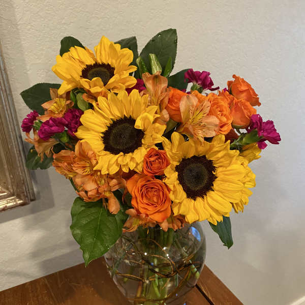 Bouquet of sunflowers, orange roses, and magenta flowers in a glass vase