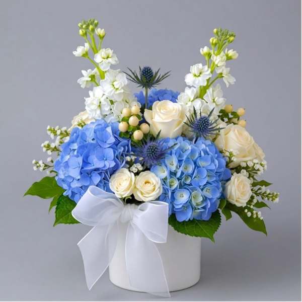 Blue hydrangeas and white roses in a white hatbox with a ribbon
