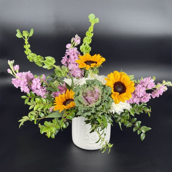 Sunflower and pink flower arrangement in a white ceramic vase